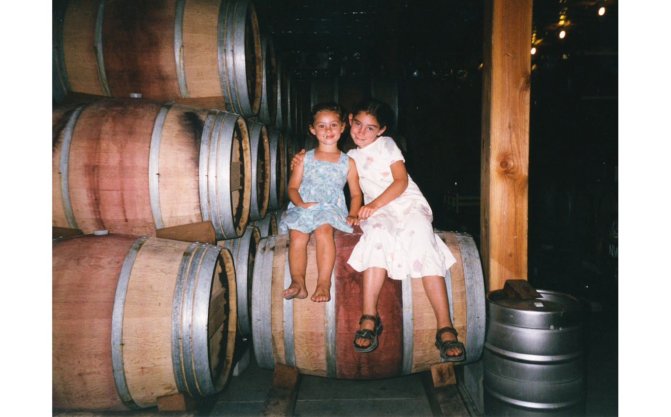 Grace and Rose Corison Martin sitting on a wine barrel in the barrel room at Corison Winery.