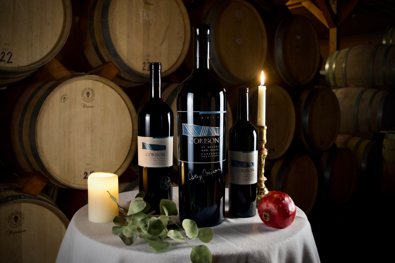 3-liter bottle of Corison Napa Valley Cabernet with label and Cathy Corison's signature etched and painted on the bottle, flanked by a magnum and 750ml bottle on a holiday table in the winery barrel room.