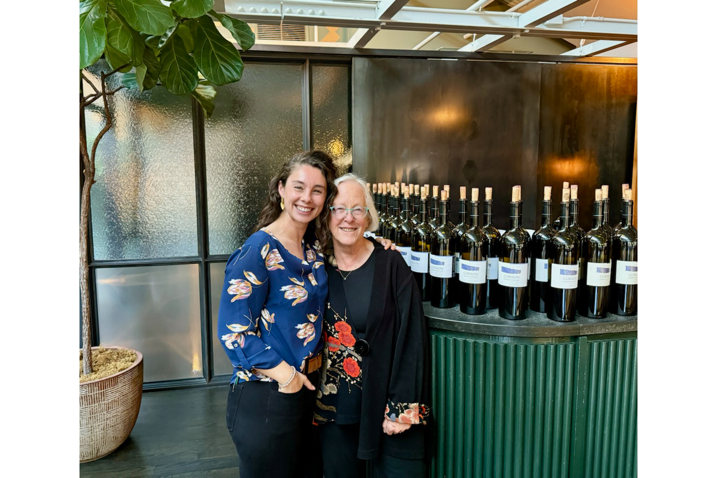 Grace Corison Martin and Cathy Corison at a Kronos 25th Anniversary Celebration, standing in front of a lineup of Kronos Magnums