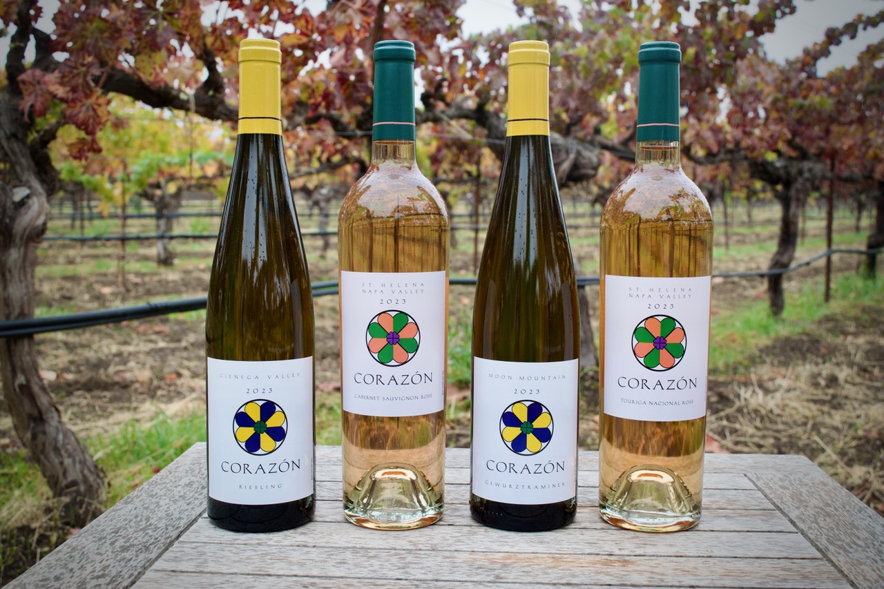 The four 2023 Corazón wines - Riesling, Cabernet Sauvignon Rosé, Gewürztraminer, and Touriga Nacional Rosé, out in Kronos vineyard under vines with leaves turning burgundy.