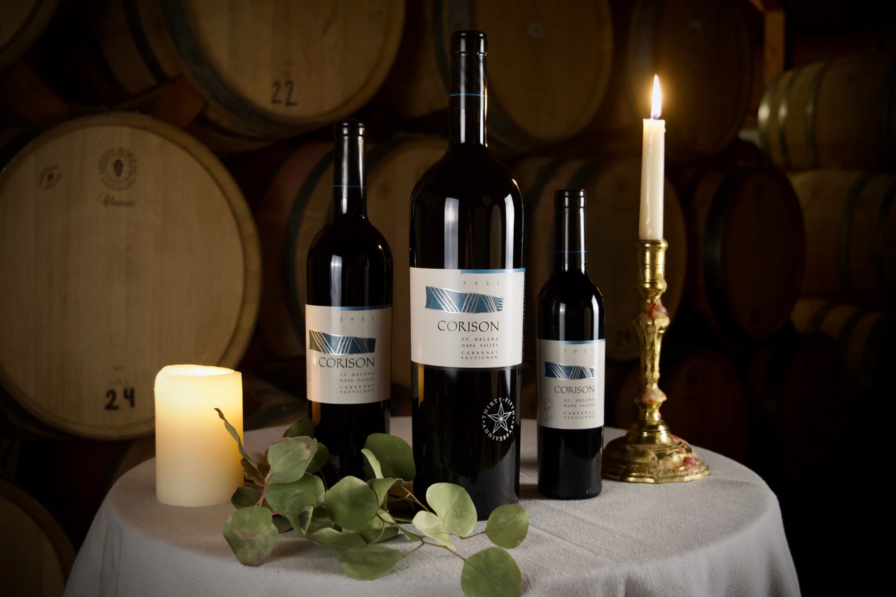 Magnum of the 2021 Corison Napa Valley Cabernet with the anniversary star etched on the bottle, flanked by 750ml and 375ml bottles on a holiday table in the winery barrel room.